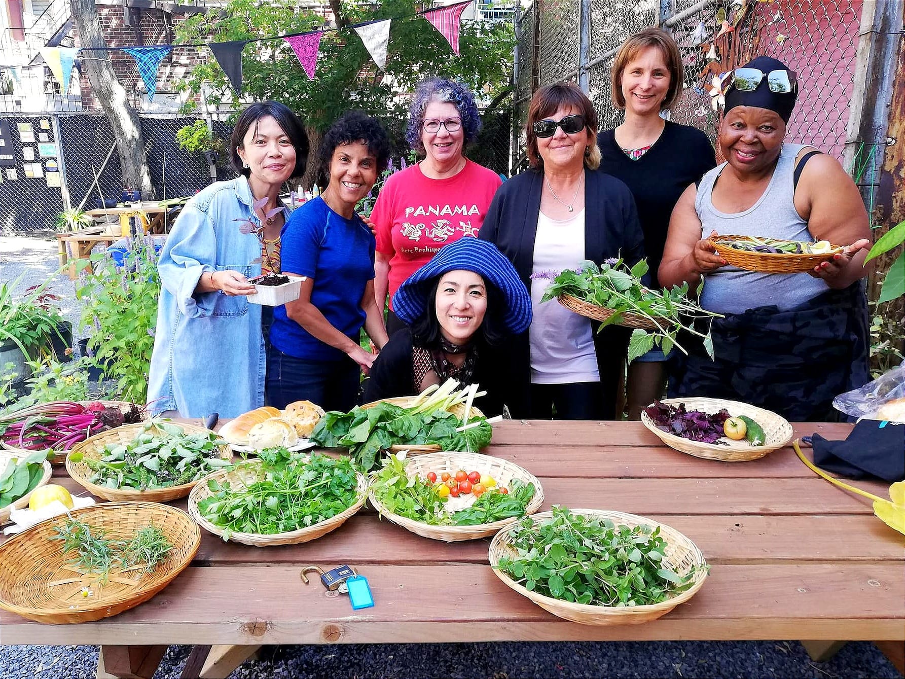Sept femmes posent dehors, derrière une table sur laquelle reposent des aliments cultivés.