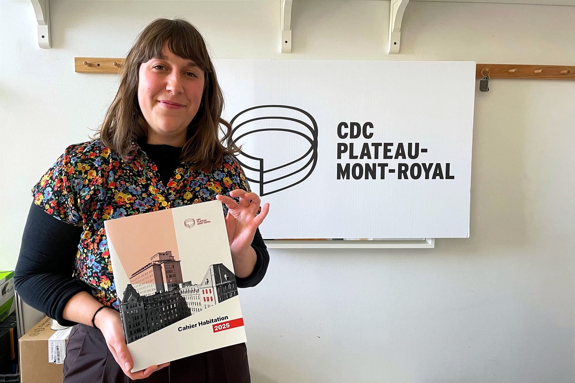 Mme Hélie-Martel tient le document dans ses mains, devant une affiche de la CDC. 