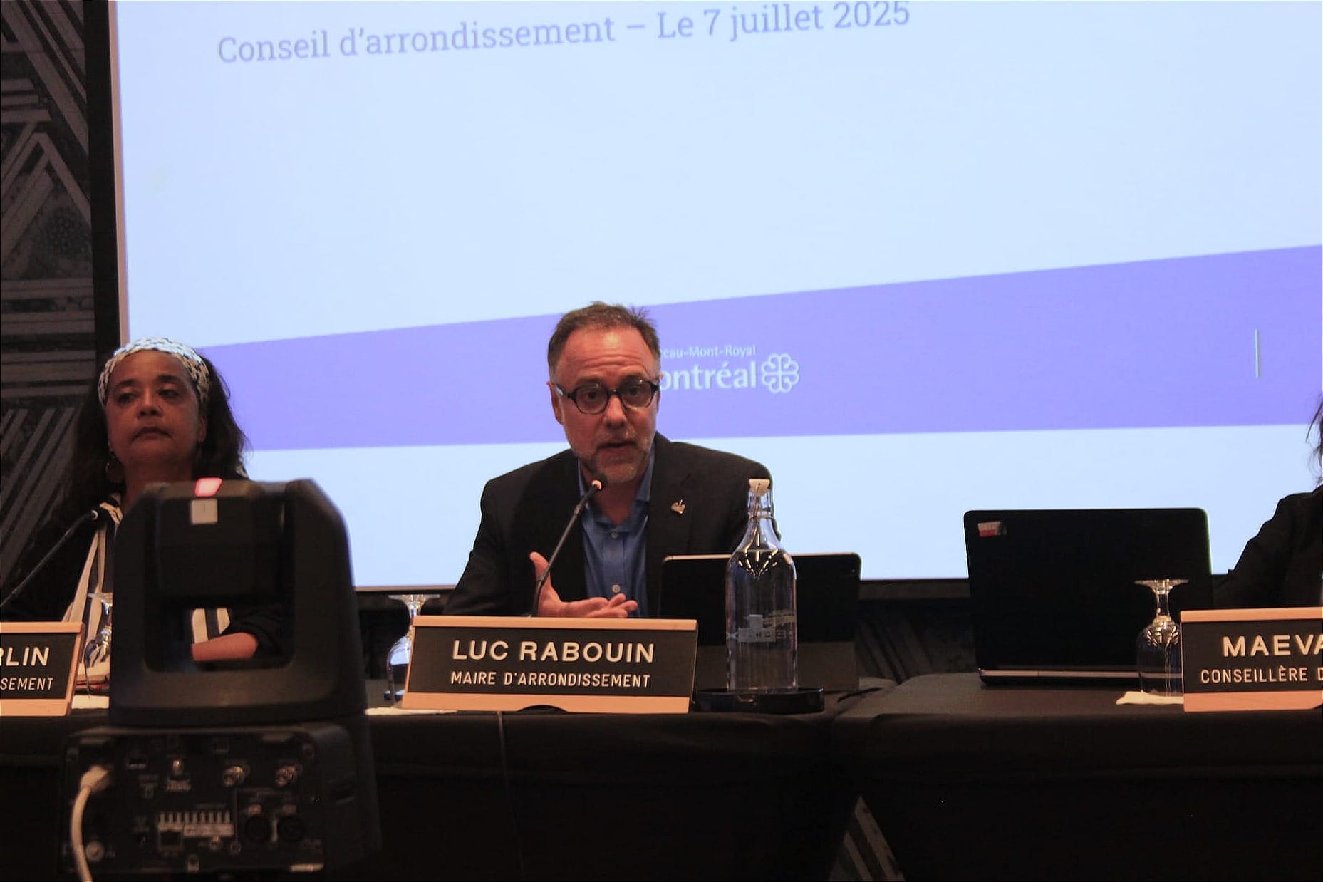 M. Rabouin est assis à la table des conseillers et parle dans son microphone pendant la séance ordinaire du conseil d'arrondissement.