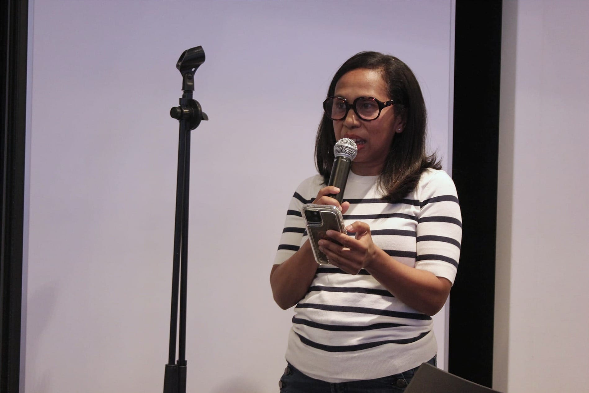 Mme Rajaonina, debout, tient un microphone d'une main et sont téléphone de l'autre.