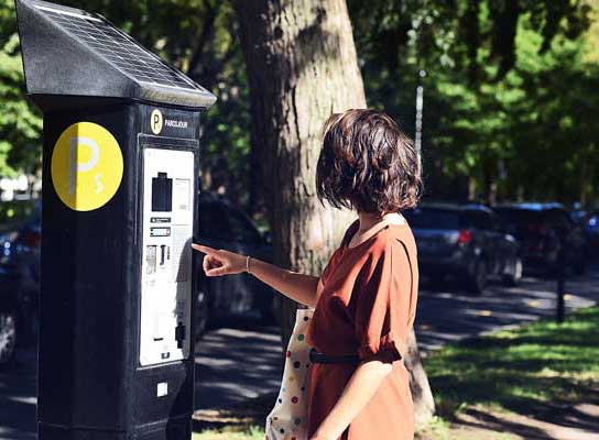 Une femme pitonne sur la borne parcojour, munie d'un symbole «P» blanc dans un cercle jaune.