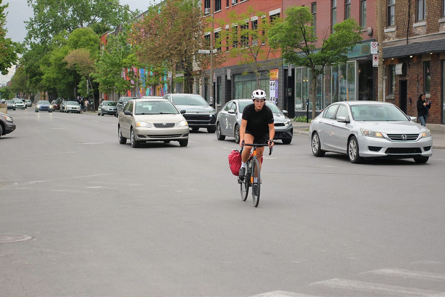 Une cycliste accompagnée des quelques voitures traverse la rue Bernard en se dirigeant vers le nord sur le boulevard Saint-Laurent. 