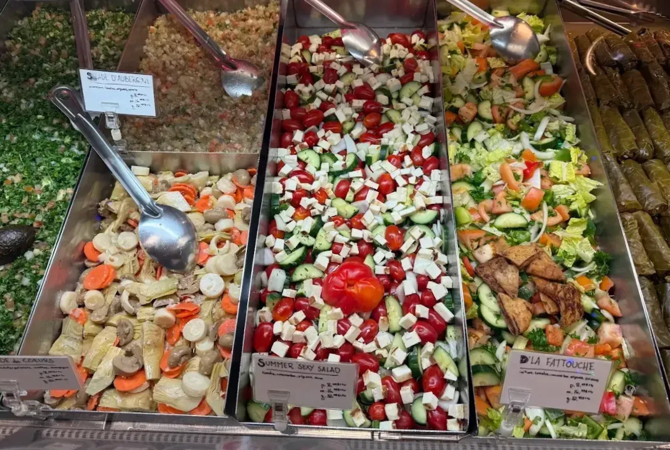 Cette photo présente un comptoir avec six salades différentes, dont une aux artichauts, une aux aubergines, une de style "Fattouche" et des feuilles de vigne farcies.