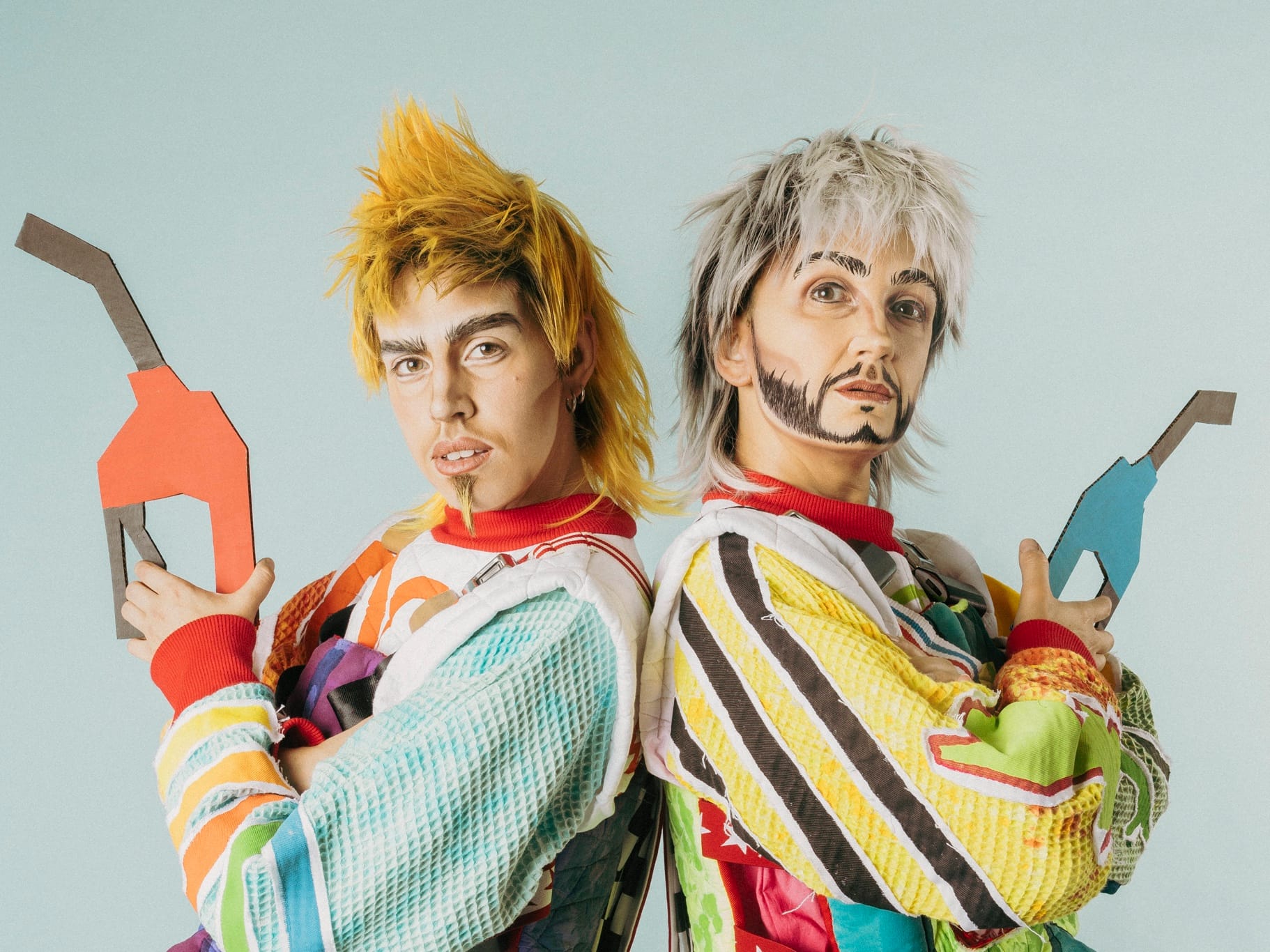 Deux drag kings tiennent des fausses pompes à essence en carton et se tiennent dos à dos.