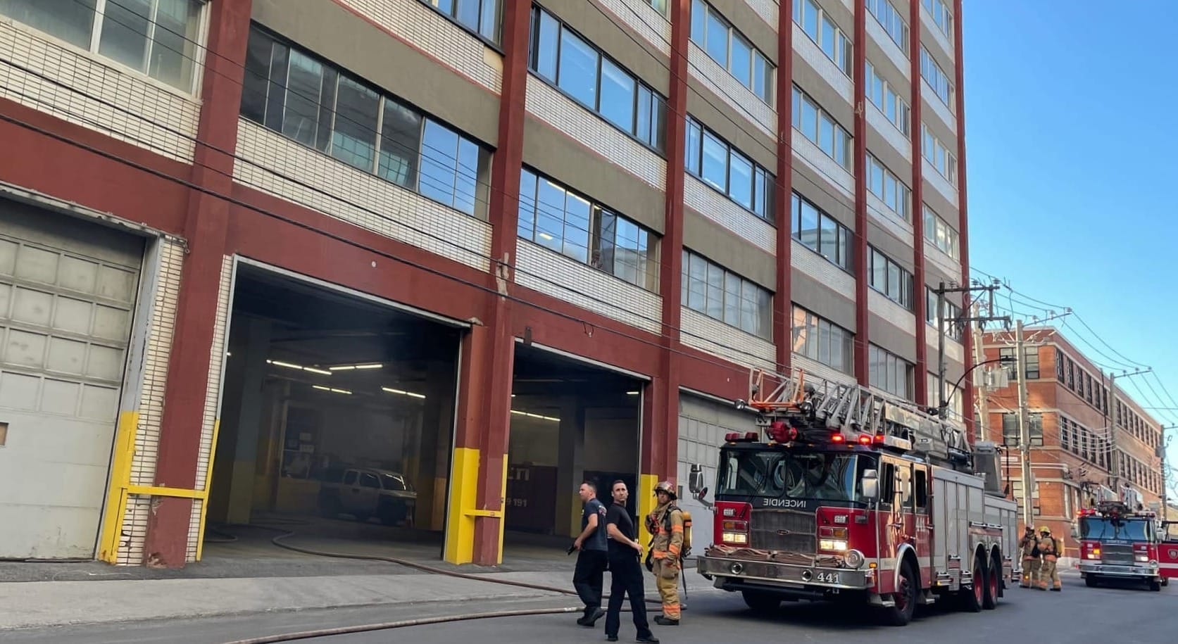 Deux camions de pompier et cinq pompiers devant une porte de garage ouverte d'où sort de la fumée.