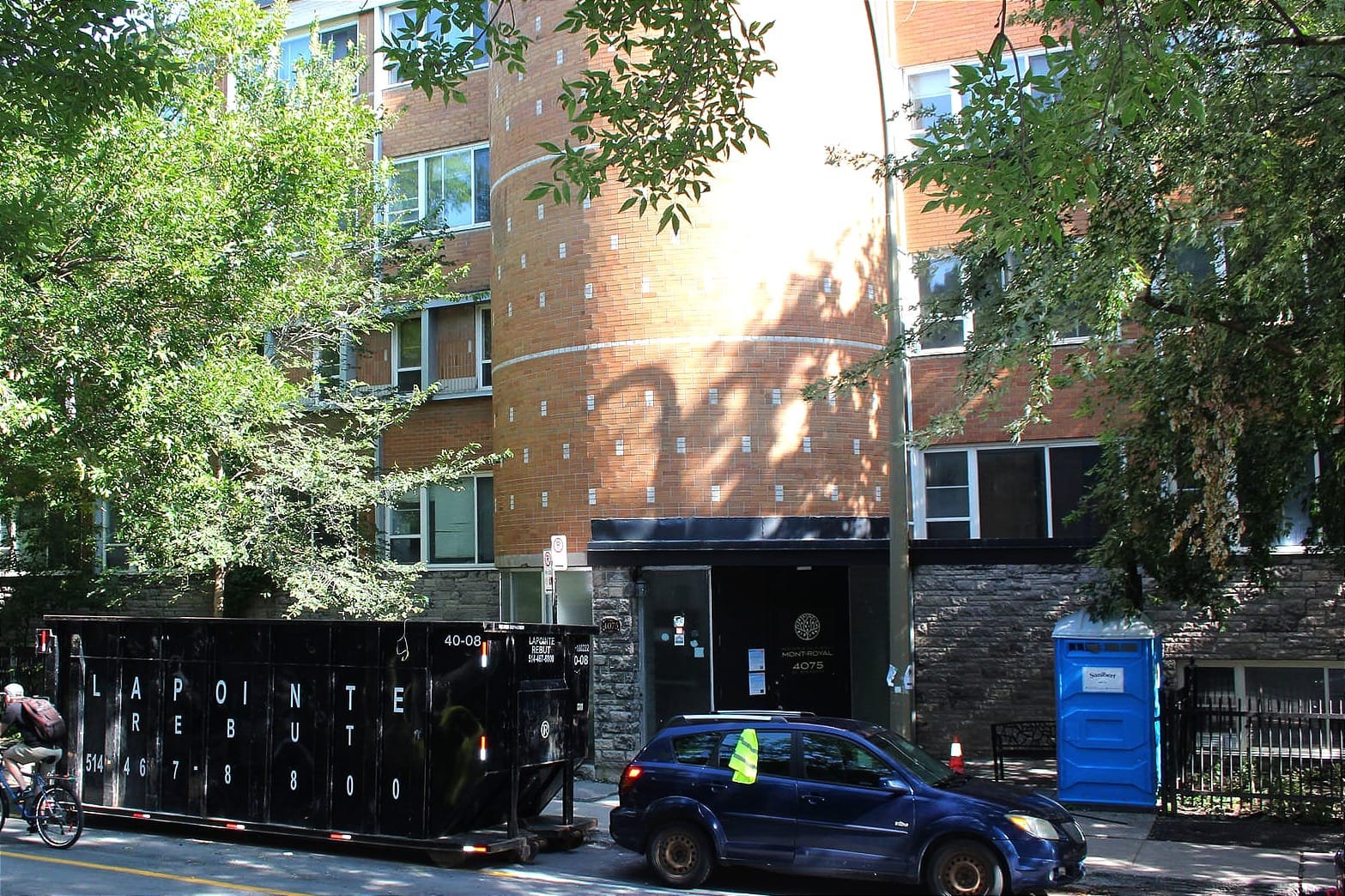 Un conteneur, le véhicule d'un travailleur de la construction et une toilette chimique se trouvent devant l'entrée du pavillon.