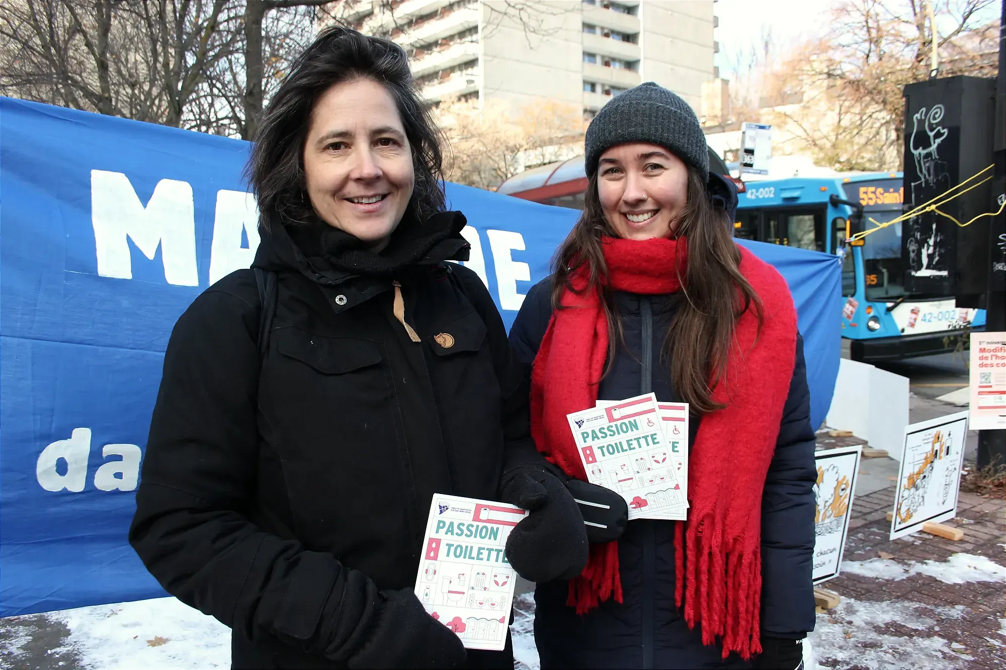 Les deux femmes tiennent leurs prospectus devant la banderole. 