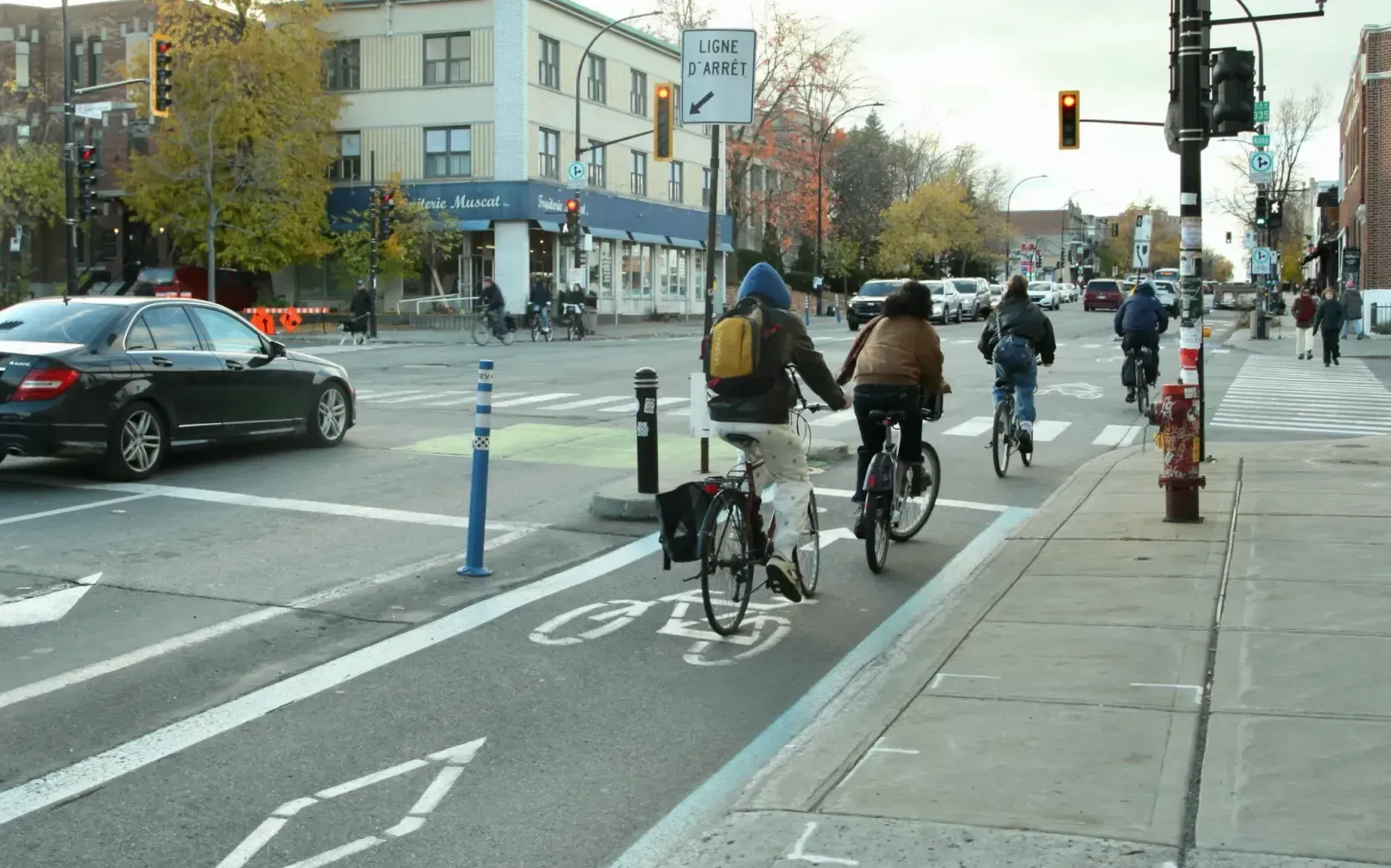 Quatre cyclistes, vus de dos, s'apprêtent à traverser le boulevard.