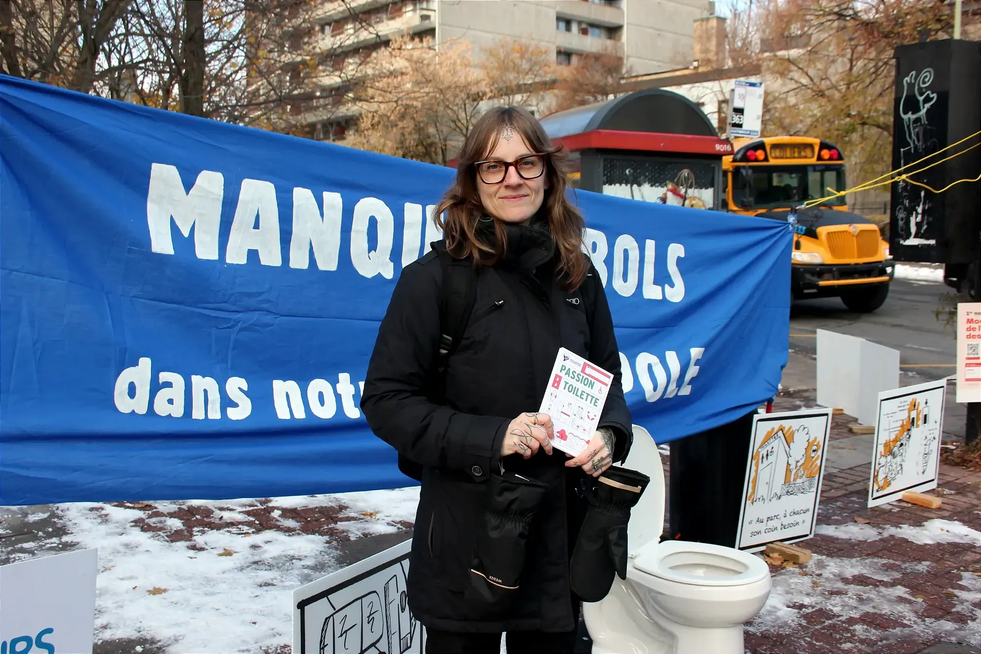 Mme Doran tient un pamphlet «Passion Toilette» devant la banderole Manque de bols dans notre métropole.