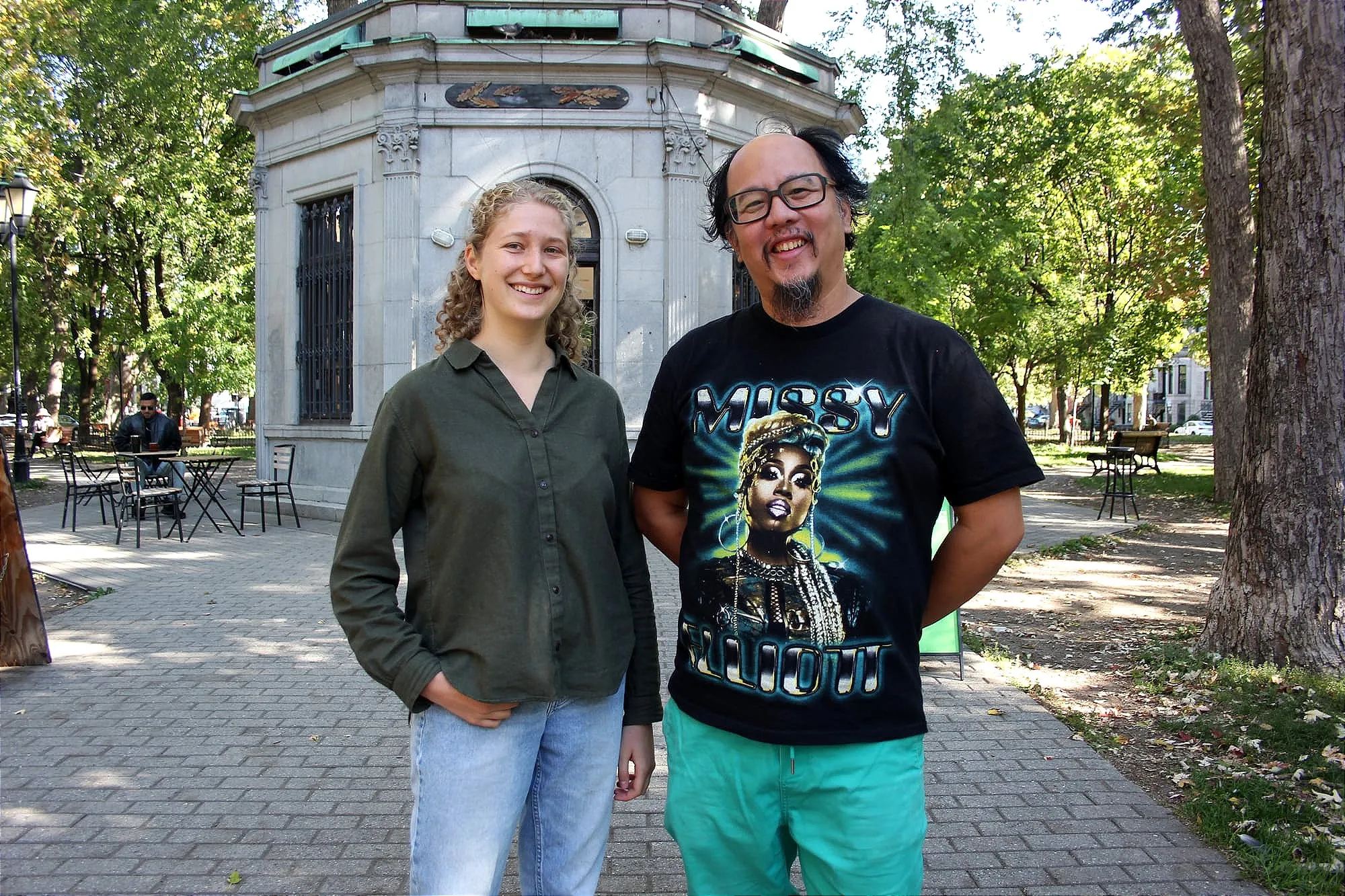 Une jeune femme au cheveux blonds et une homme aux traits asiatiques posent dans un parc, en été.