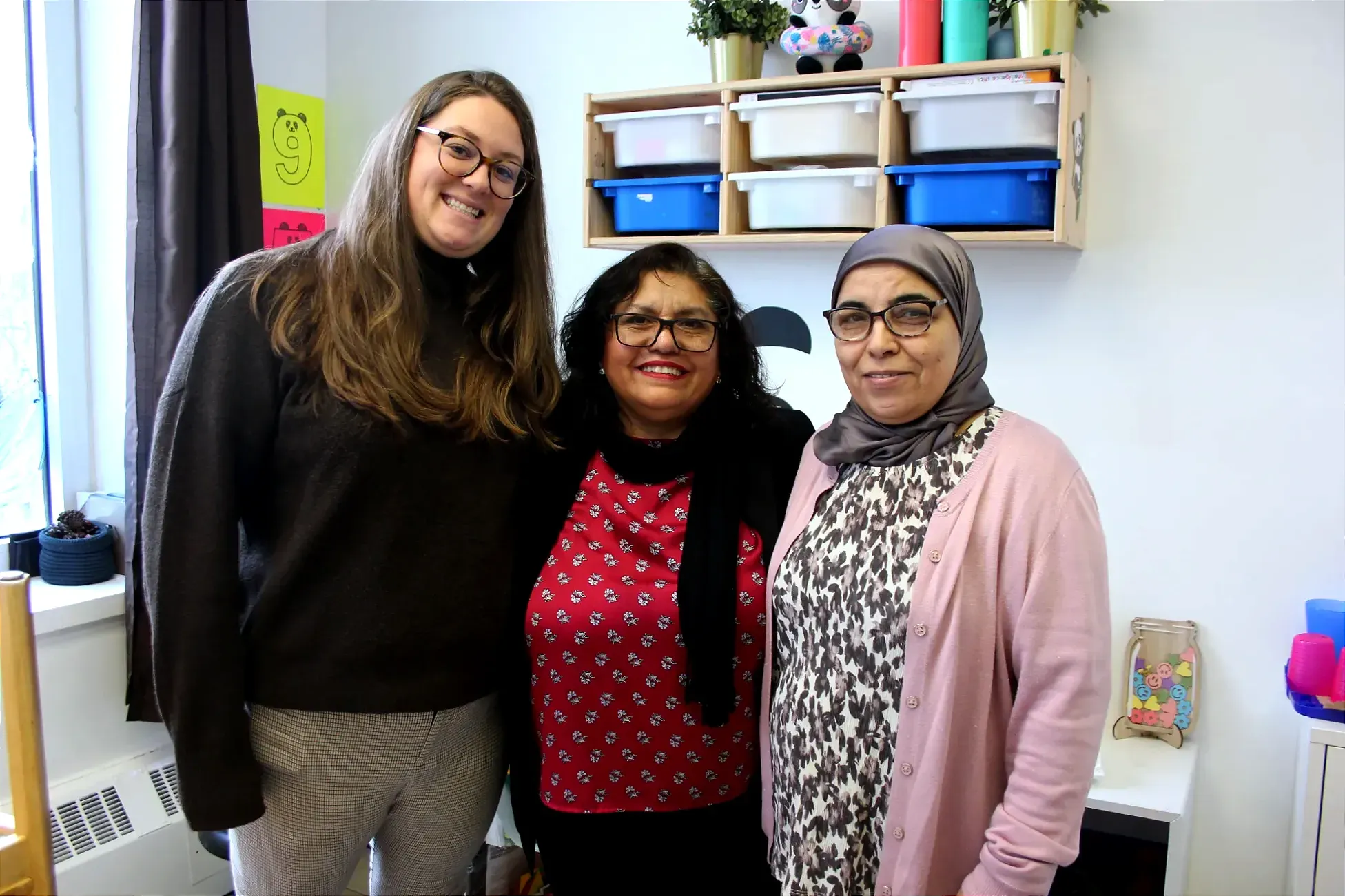 Les trois dames posent dans un local avec des objets colorés pour enfants. 