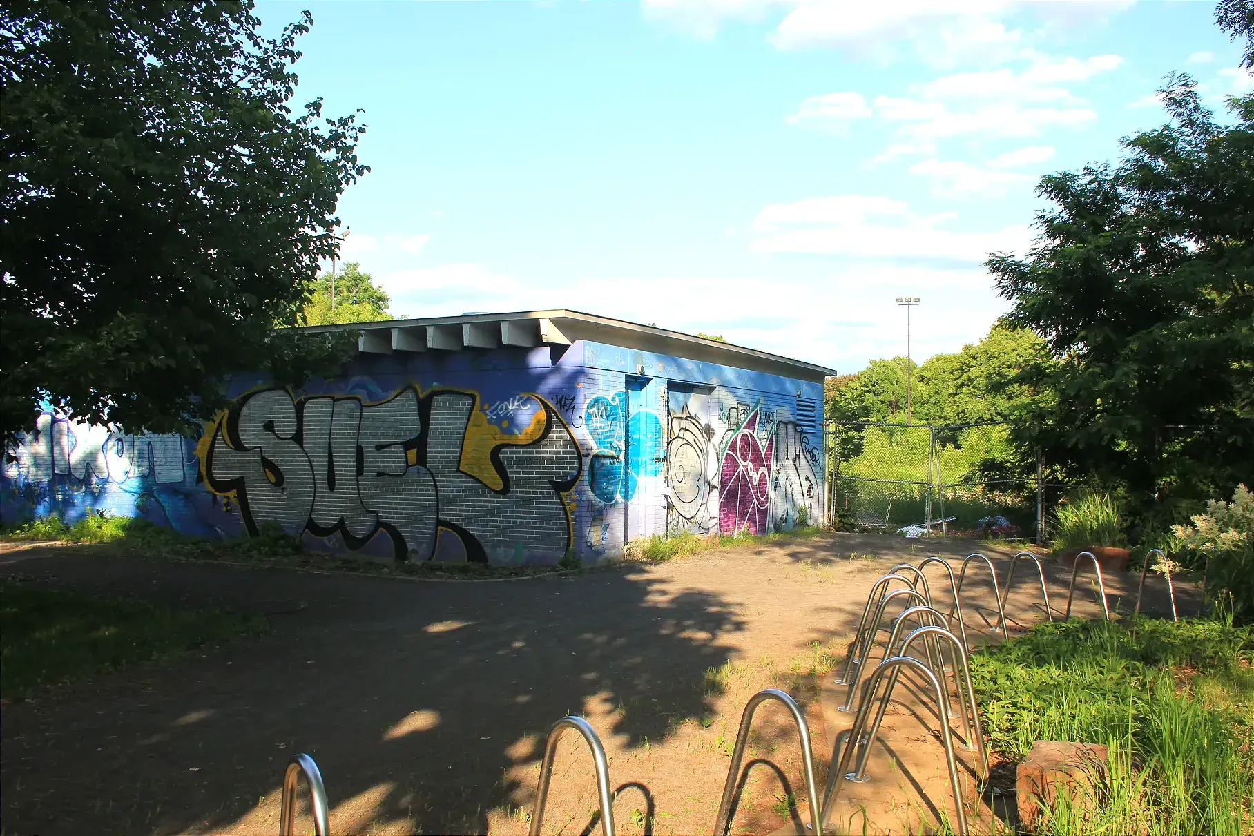 On voit l'ancien chalet, couvert de graffiti et la clôture qui entoure le terrain où se trouvait autrefois le bassin.