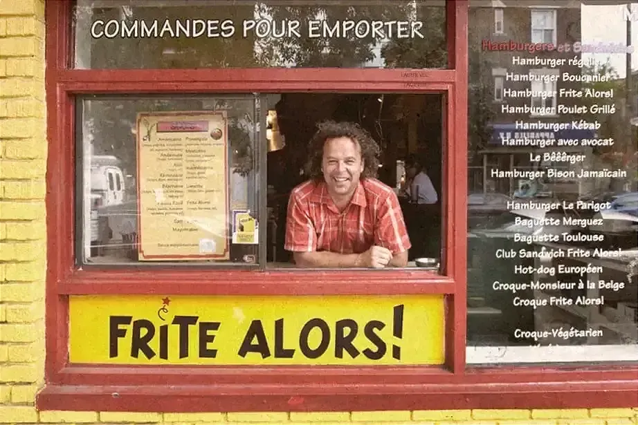 M. Jurdant sort la tête de la fenêtre. On voit le menu à sa gauche écrit sur la fenêtre et la brique est encore de couleur jaune.