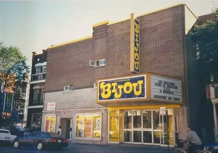 On voit la bâtisse avec les grandes affiches du Cinéma Bijou et une cycliste qui roule devant. 