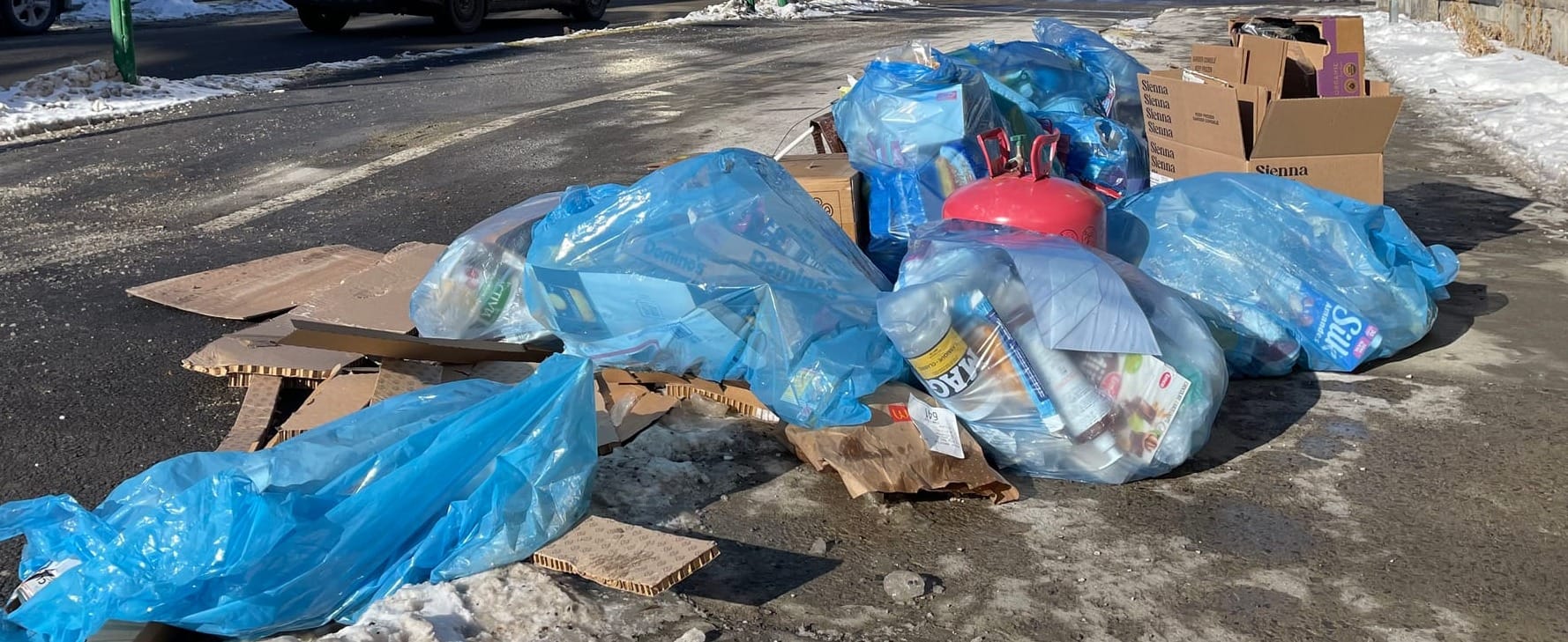 Une image en plan rapproché de sacs de recyclage pleins et de boîtes de carton, en bordure d'une rue du Plateau.