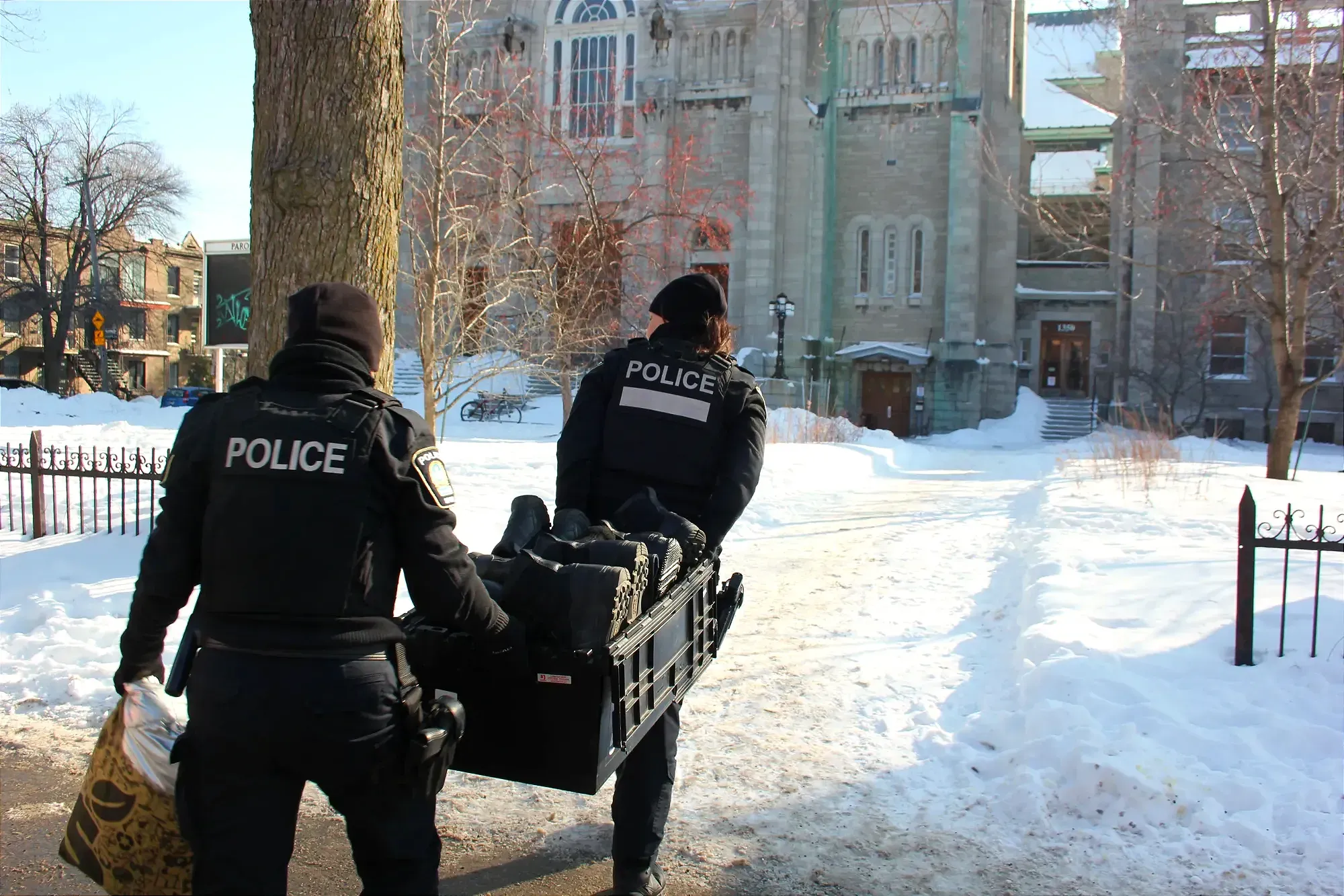 Les policières se dirigent vers l'église Saint-Stanislas-de-Kostka transportant une boîte en plastique. 