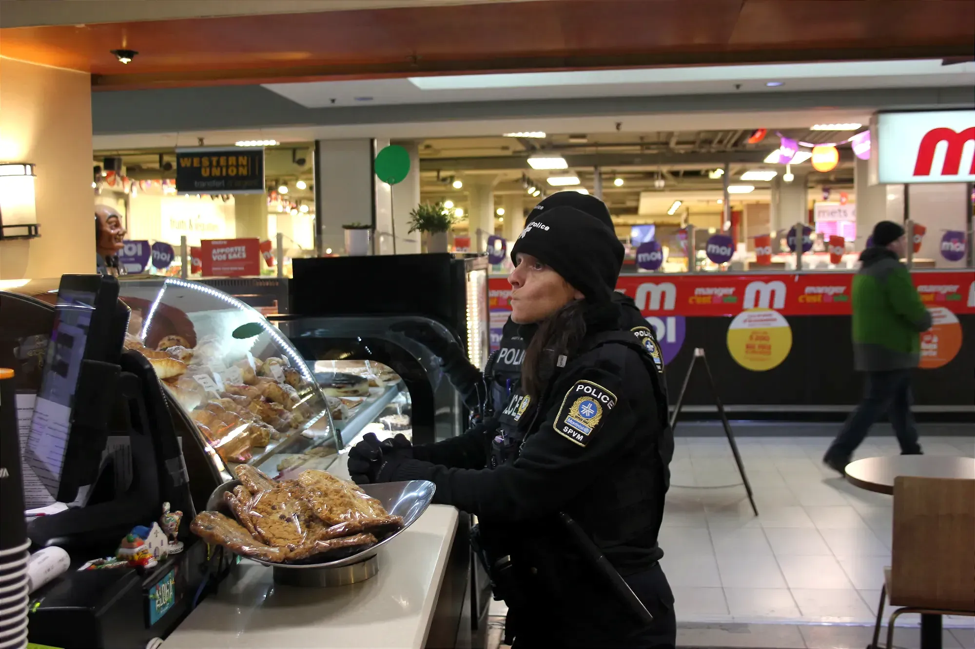 Véronique Brazeau est accotée sur un comptoir, à côté d'un présentoir de biscuits. L'agente Morin