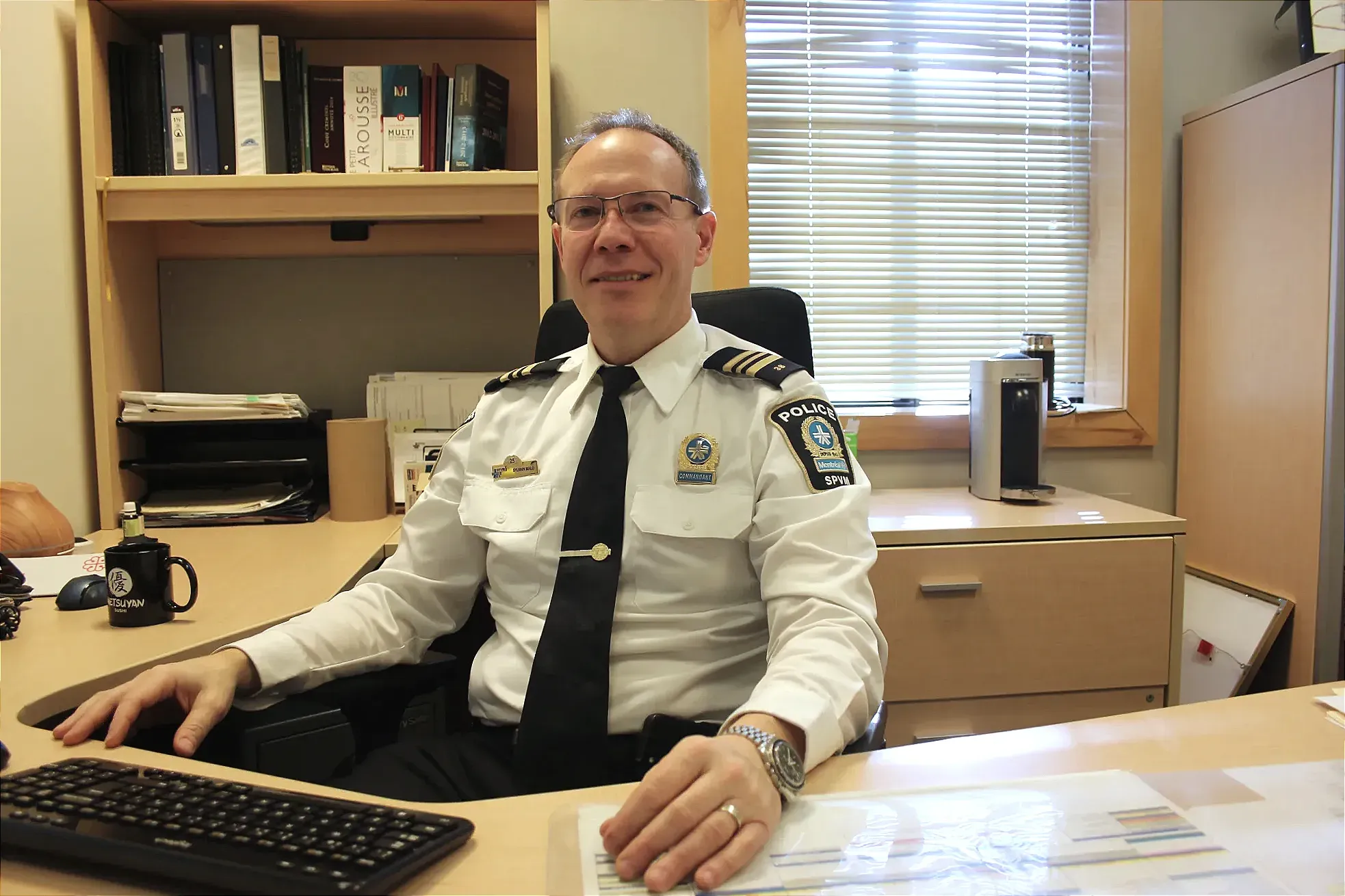 Le commandant Malo pose, souriant, en fixant la caméra, les mains sur la surface de son bureau.