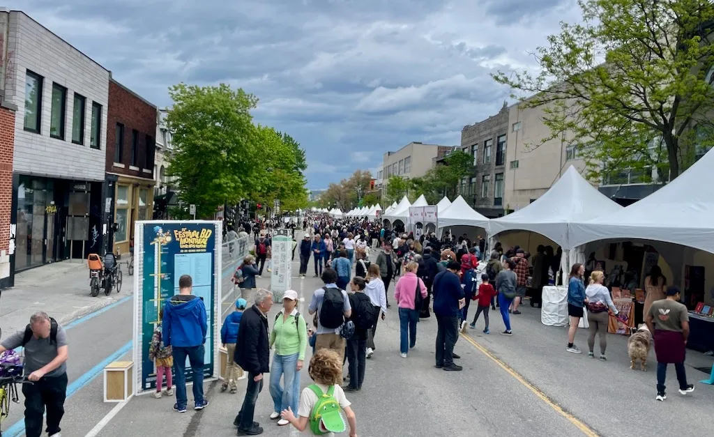 Une photo sous un ciel nuageux, en début d'été, avec une vue de la rue remplie de gens et de kiosques.
