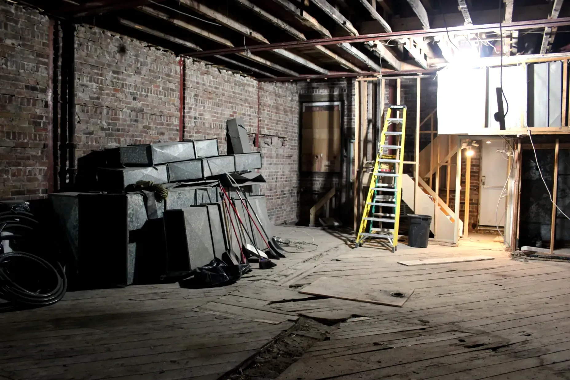On voit des pièces (tuyaux, conduits d'aération, balais, etc.) empilés près du mur. Le plancher, les murs et le plafond ne sont pas recouverts.