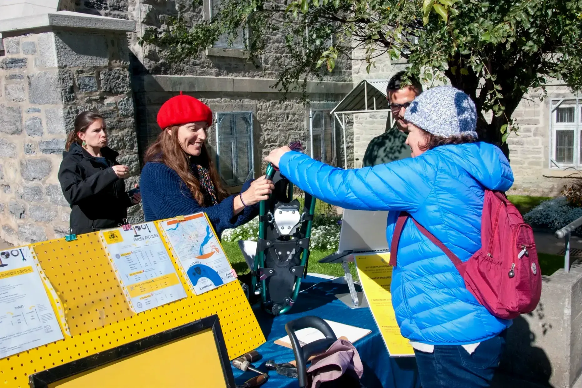 Une femme remet des raquettes à une autre dame. Les deux se trouvent des côtés opposés d'une table placée à l'entrée du site de la Cité-des-Hospitalières.