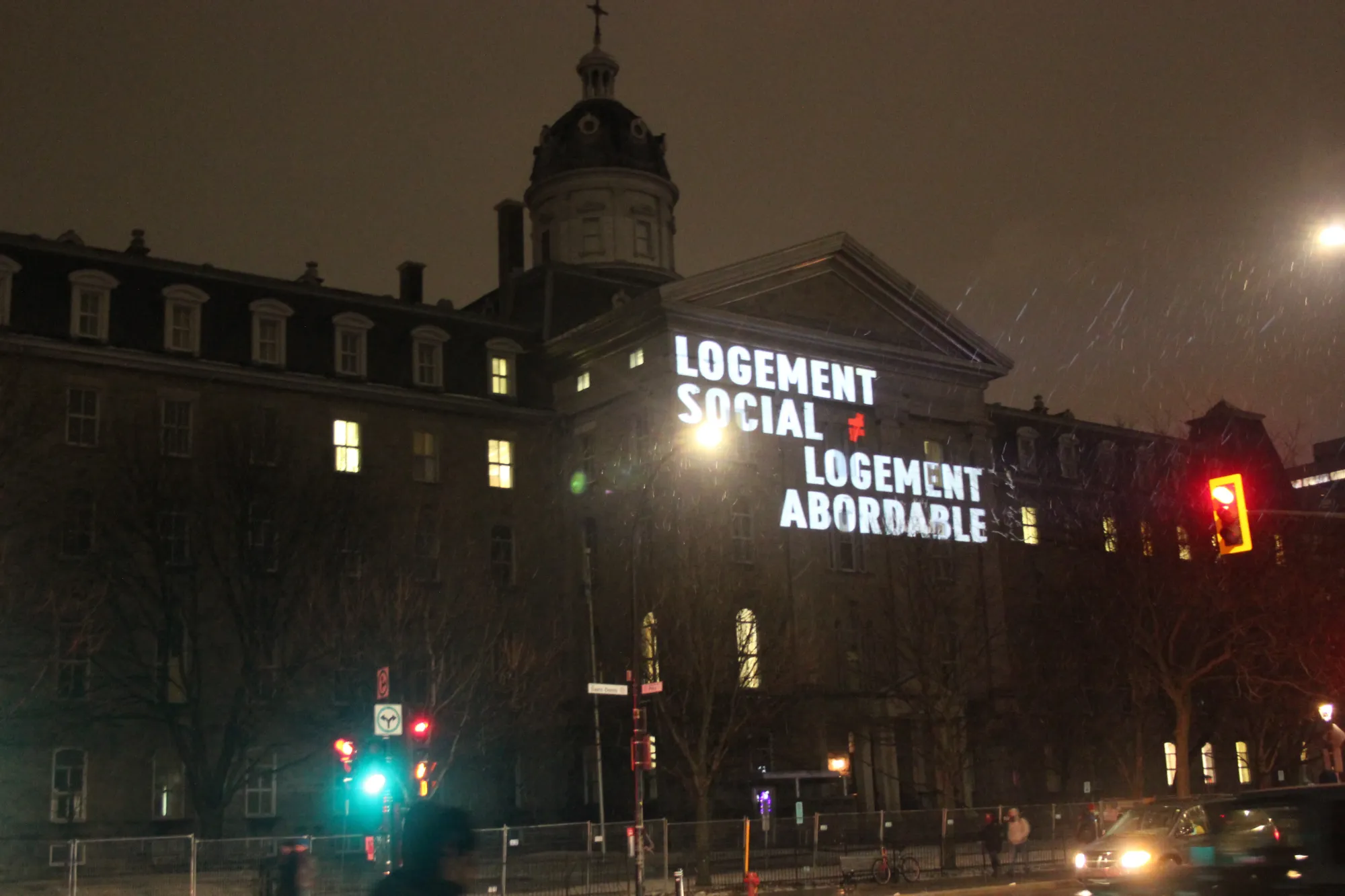 Sur la façade ouest du bâtiment, dans la nuit, on peut lire le texte: Logement social n'égal pas logement abordable