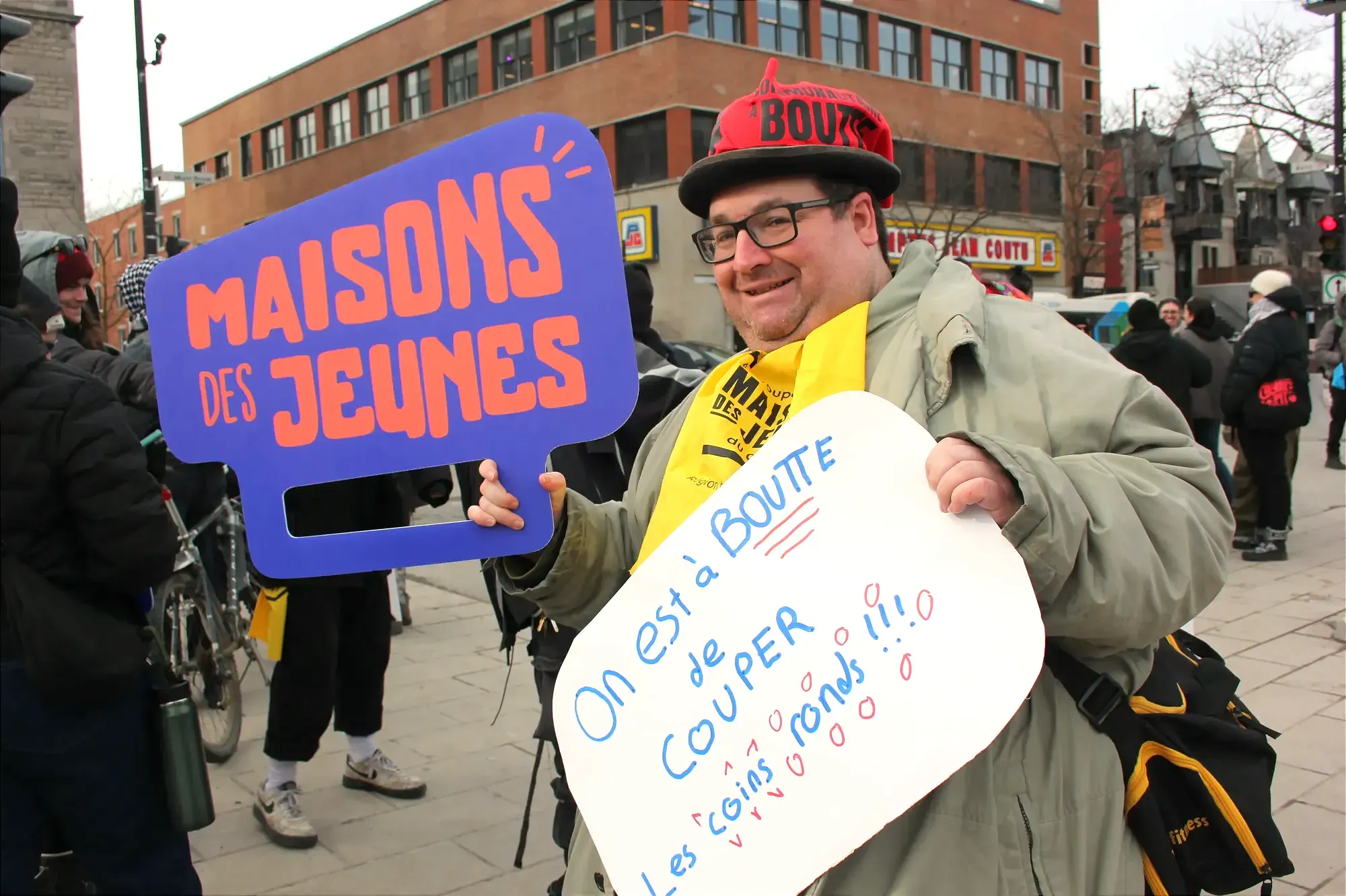 M. Garneau pose avec deux pancartes sur lesquelles ont peut lire «Maison des jeunes» et «On est à boutte de couper les coins ronds!!!»