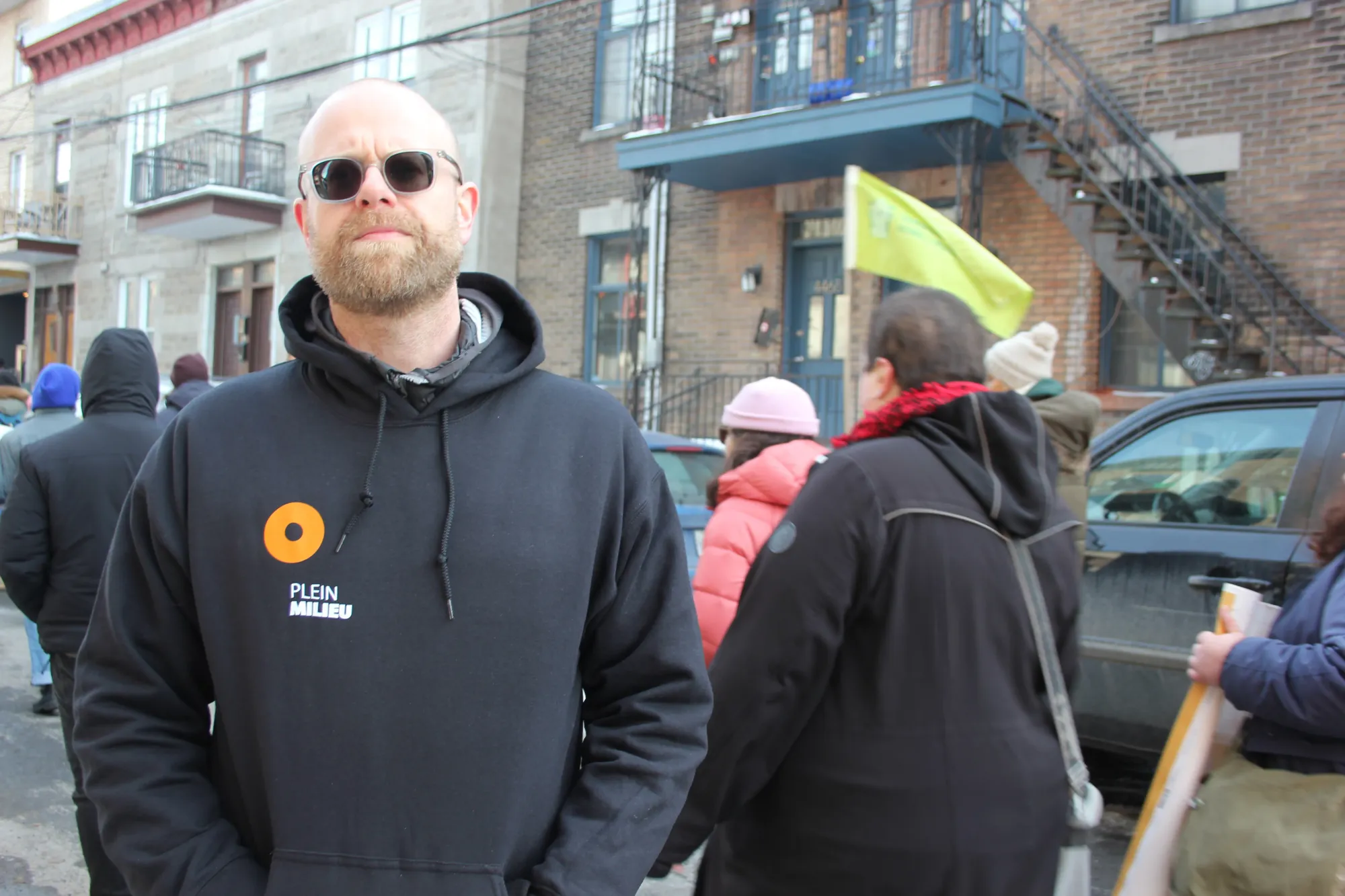 M. Quirion pose pour la caméra alors que des manifestants défilent derrière lui.