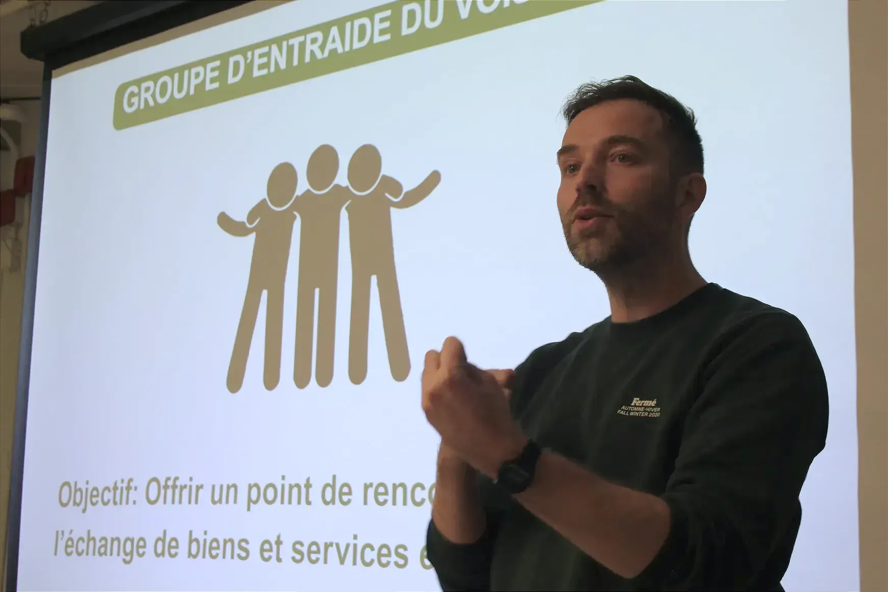 M. Marin est en pleine explication, devant l'écran sur lequel est projeté l'image liée au groupe d'entraide du voisinage.