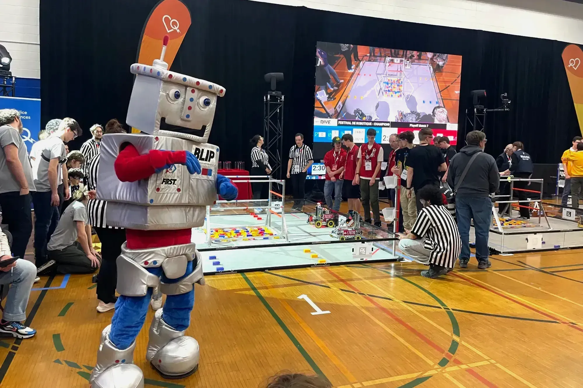 Une mascotte robot danse devant les terrains de compétition.