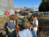 Six personnes sont debout au milieu d'un terrain vague en milieu urbain.