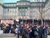 On voit des manifestants regroupés aux alentours du trottoir devant le bâtiment patrimonial de la rue University.