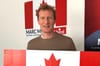 M. Miller dans son bureau de circonscription, tenant un drapeau canadien et posant devant ses pancartes électorales.
