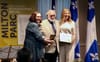 Les trois posent pour les photos sur une scenette, montrant une médaille et un certificat, devant des drapeaux du Québec.