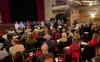 Une salle avec des chaises et des dizaines de personnes assises, face à neuf candidats et une présentatrice.