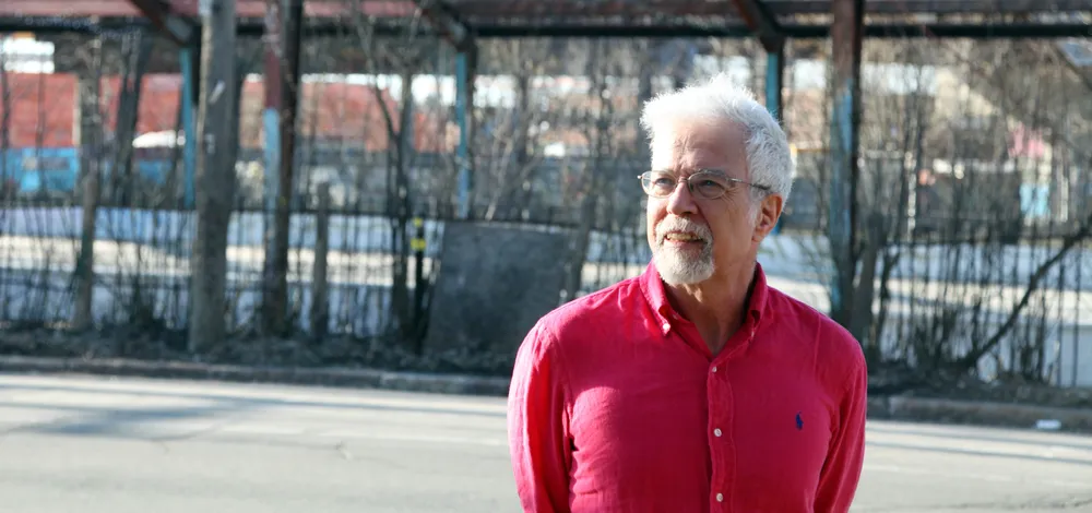 Cette photo présente le haut du corps de Joshua Wolfe en chemise rose foncée, posant devant l'entrepôt 77.