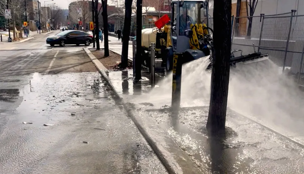 Un véhicule de nettoyage arrose un trottoir de l'avenue Laurier de multiples jets d'eau.