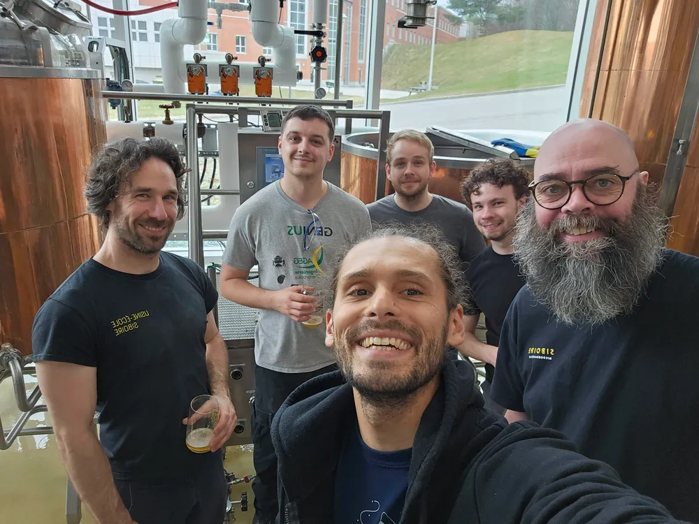 Six personnes posent devant des cuves de brassage.