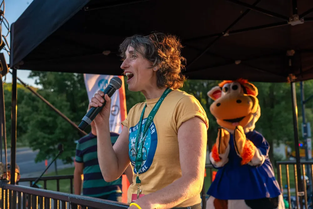 Marianne Giguère en été, micropone à la main, sous un chapiteau, au coucher du soleil.
