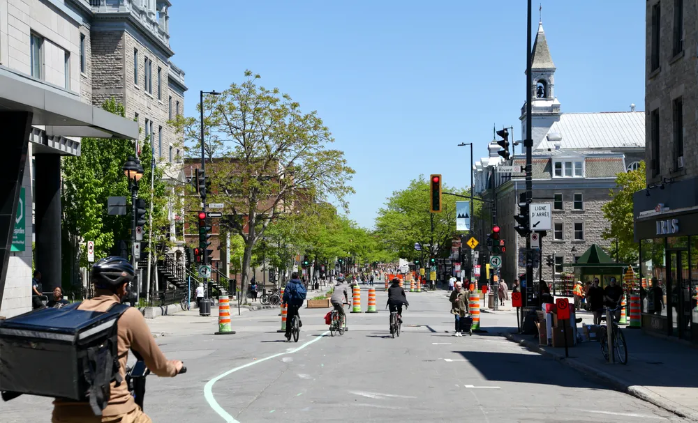 Une photo qui montre l'avenue Mont-Royal vers l'est, à partir de la rue Saint-Denis. On y voit quatre cyclistes, des cônes oranges et quelques piétons.