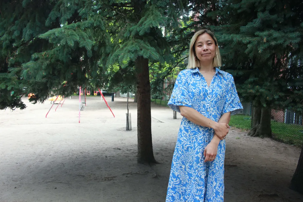 Cathy Wong est debout dans un parc, l'été, avec des jeux pour enfants.