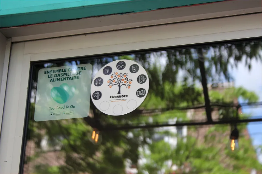 Un voit l'autocollant sur le haut de la vitre de la porte d'entrée et des réflexions des arbres et autres objets qui se trouvent à l'avant.