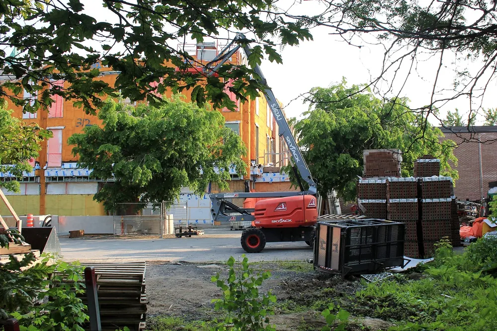 On voit les briques à droite, un chariot élévateur au centre et les surfaces orangées de l'école au fond de la cour.